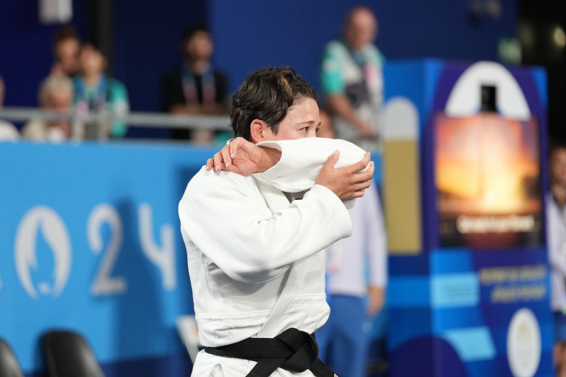 Christa Deguchi holds her arm up to her face as she reacts in disbelief to her win