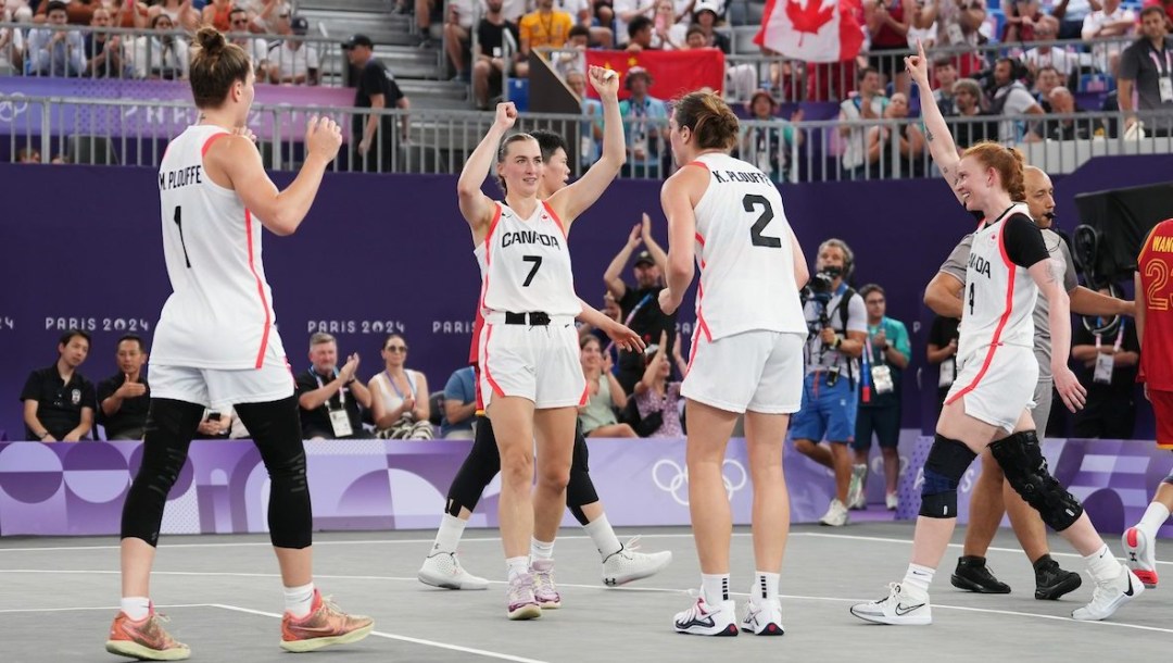 Four female basketball players in white celebrate at the end of a game