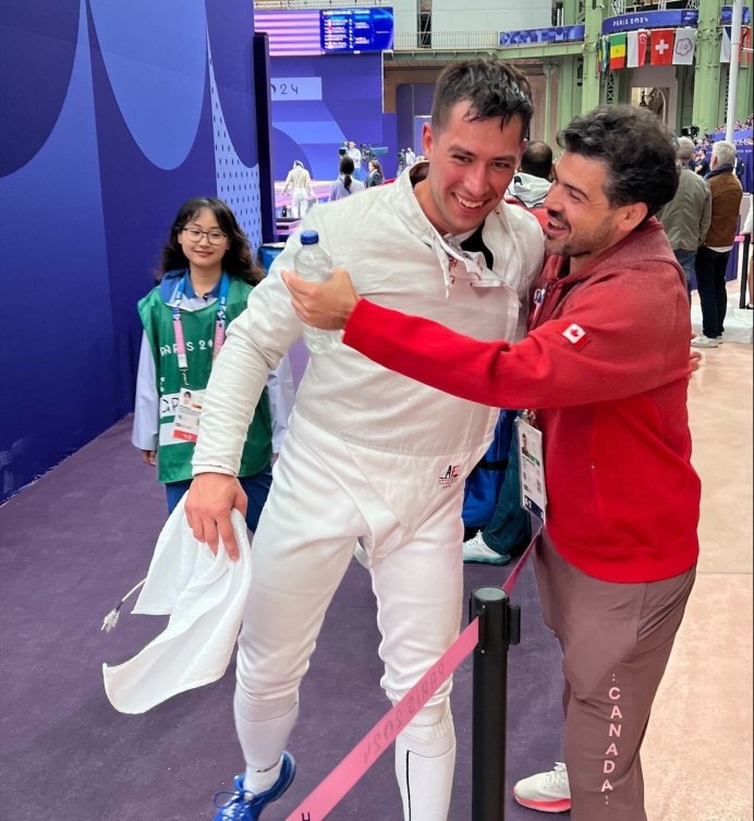 Fencer Fares Arfa gets a hug from his coach in a red outfit 