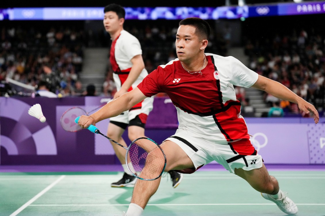 Two badminton players reach for the birdie