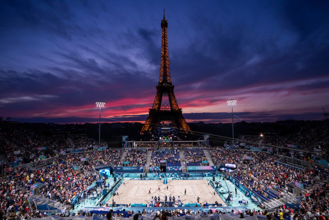 The Eiffel Tower has a beach volleyball court in front of it and a brilliant purple and pink sunset