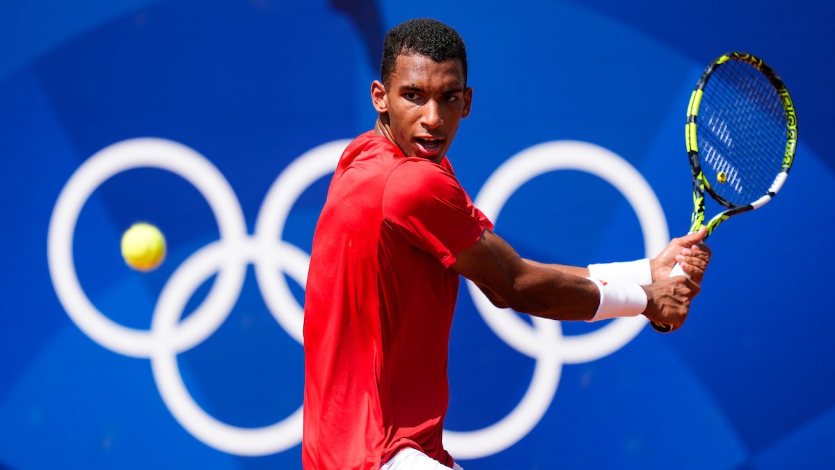 Felix Auger-Aliassime in red shit prepares to hit a ball in a tennis match