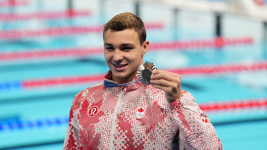 Ilya Kharun poses with a bronze medal in a red and white track suit 