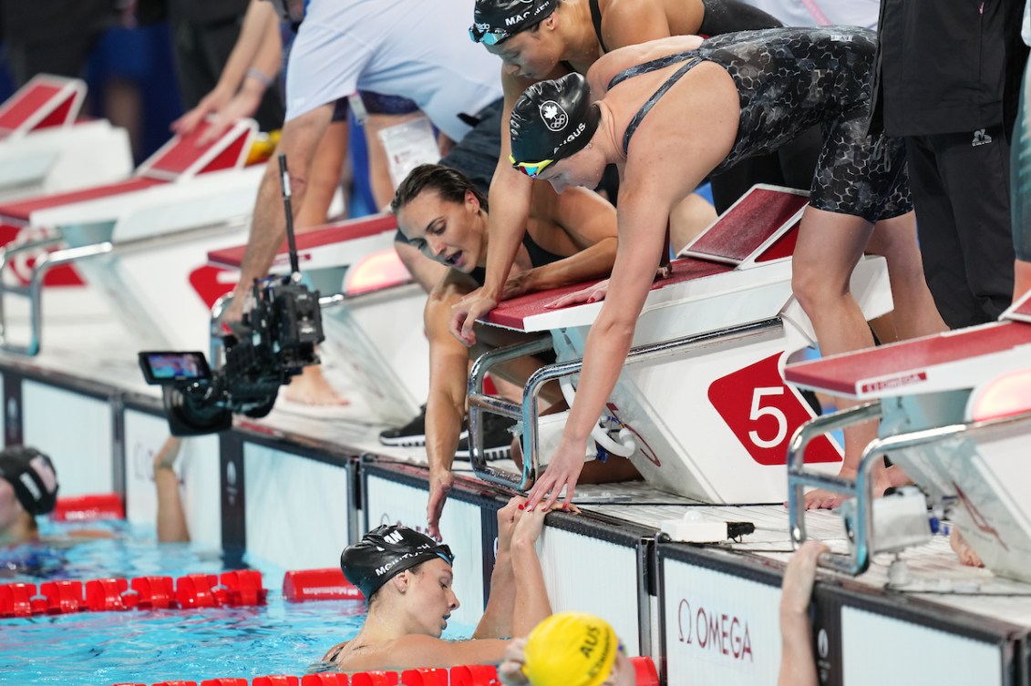 Summer McIntosh hangs off the edge of the pool as her teammates reach over to her 