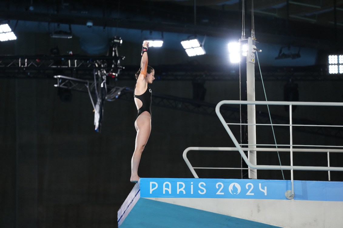 Caeli McKay in a black swimsuit stands on the edge of the 10m diving platform