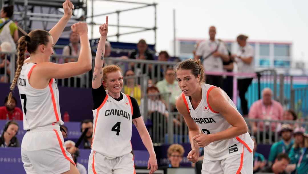 Three Canadian women basketball players in white uniforms celebrate a win