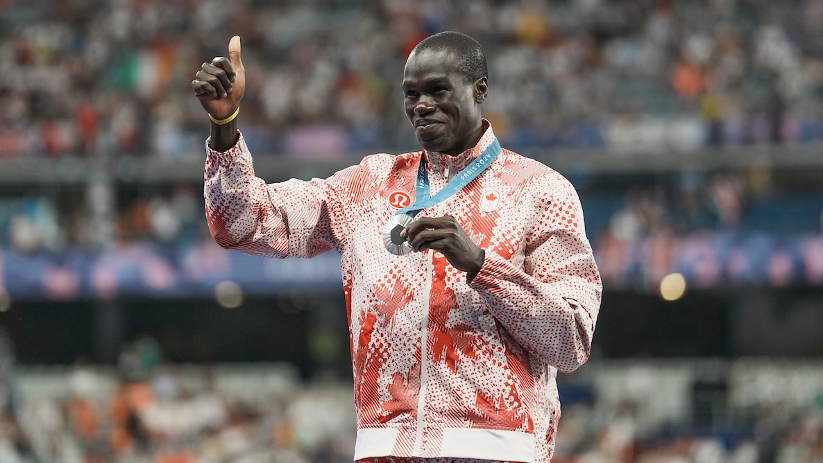 Marco Arop gives a thumbs up on the podium as he holds his silver medal