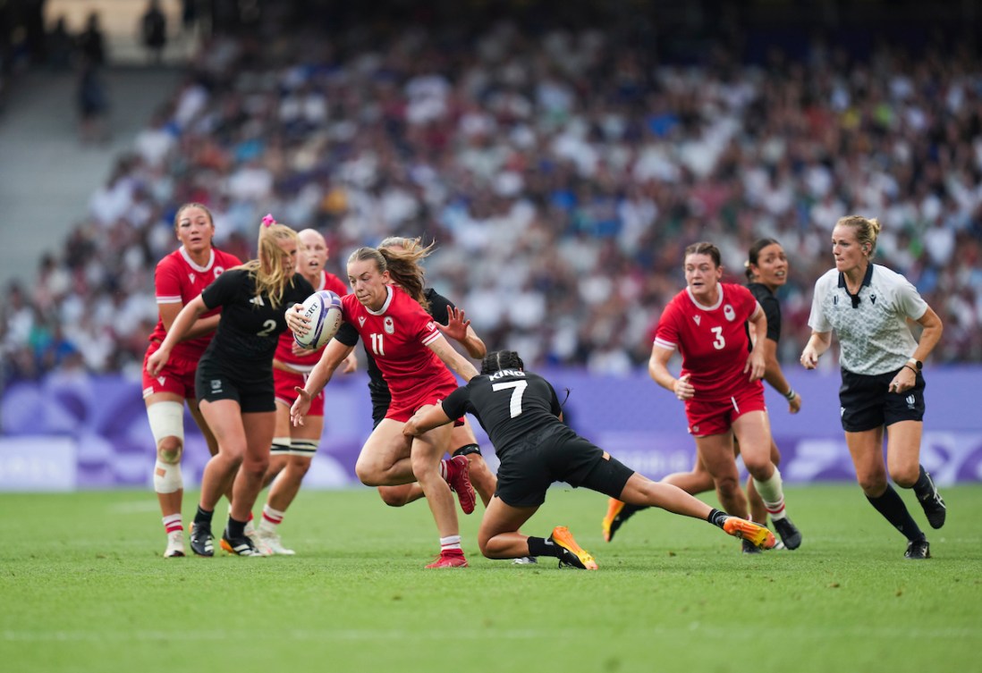 Piper Logan in red carries the ball past New Zealand players in black 