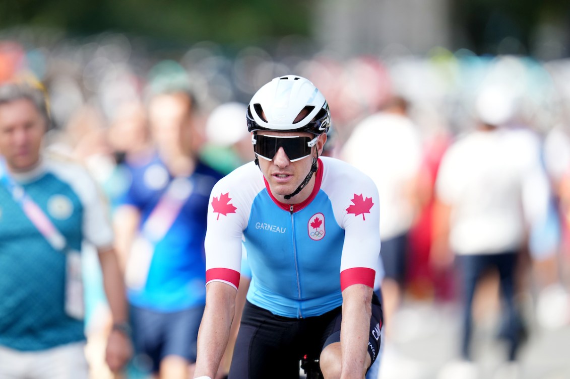 Mike Woods on his bike wearing a helmet, sunglasses and a blue jersey