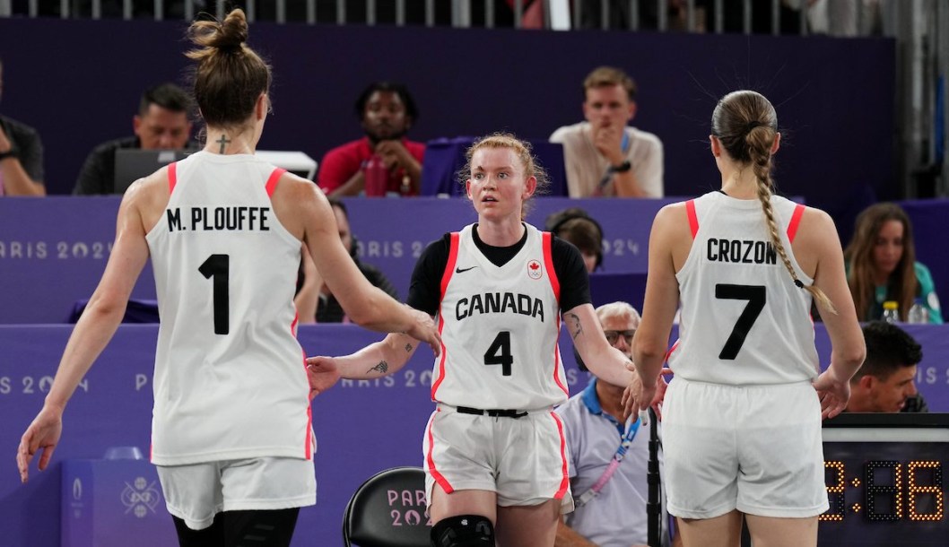 Three Canadian basketball players in white shake hands with each other