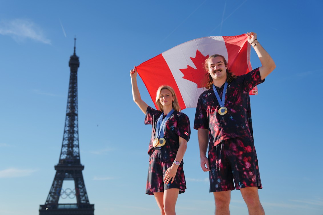 Summer McIntosh and Ethan Katzberg hold the Canadian flag above their heads in front of the Eiffel Tower 