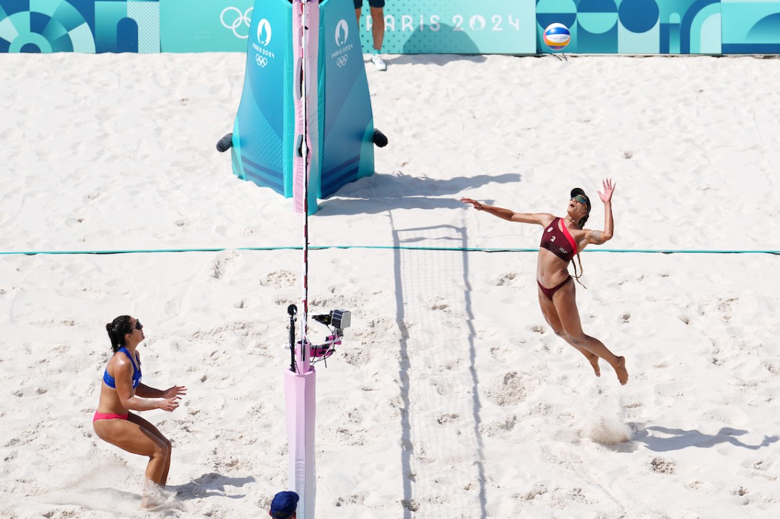 Brandie Wilkerson jumps into the air to serve on a sand court