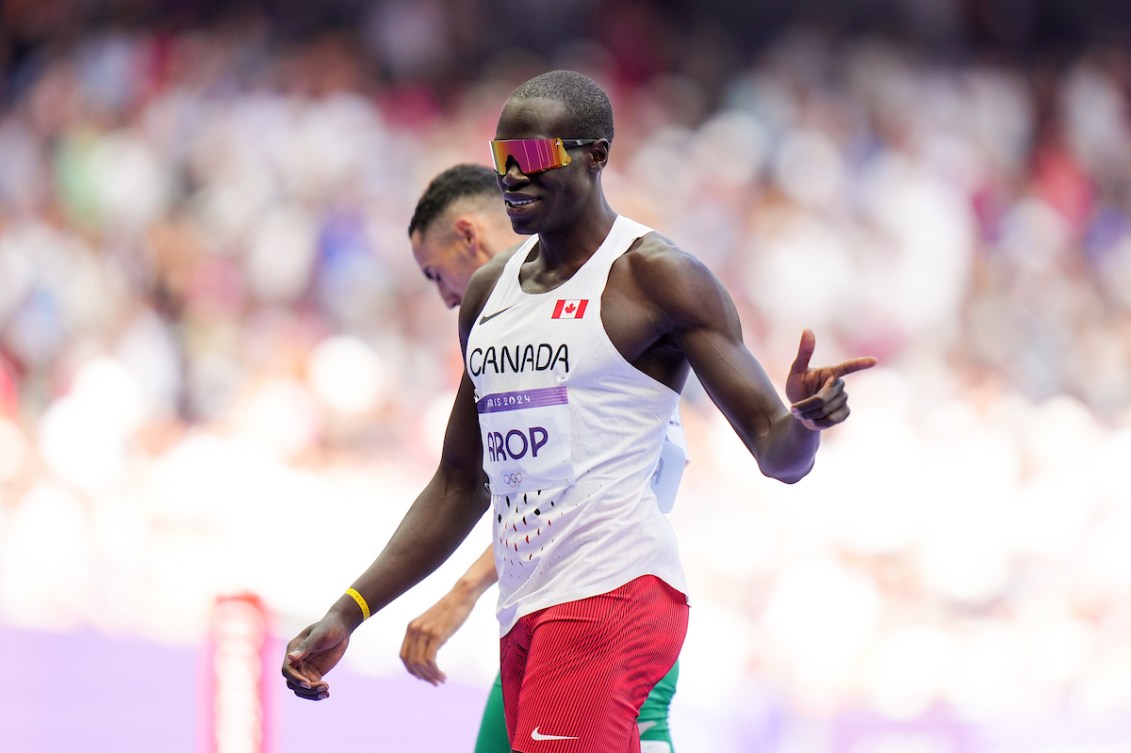 Marco Arop gives a finger gun while wearing a white singlet and sunglasses