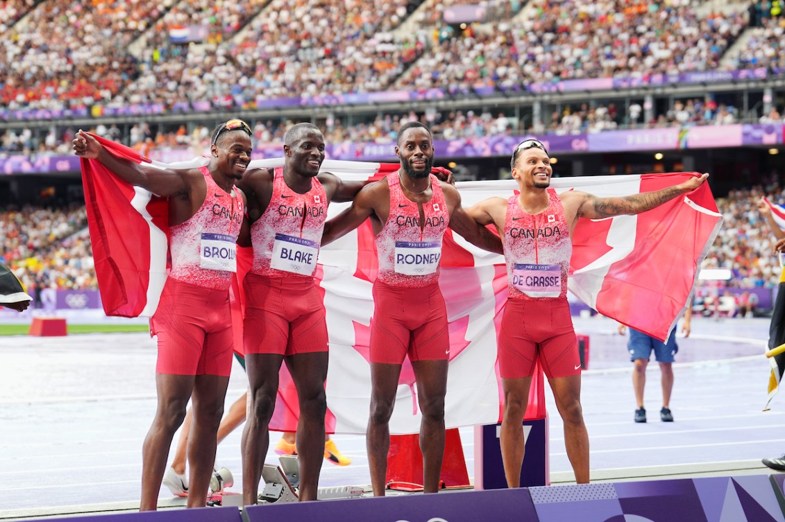 Team Canada's 4x100m relay team poses with Canadian flags draped over their shoulders