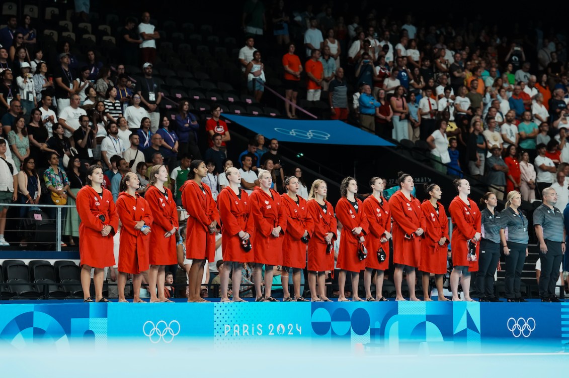 Team Canada's water polo team wears red robes and stands on the side of the pool