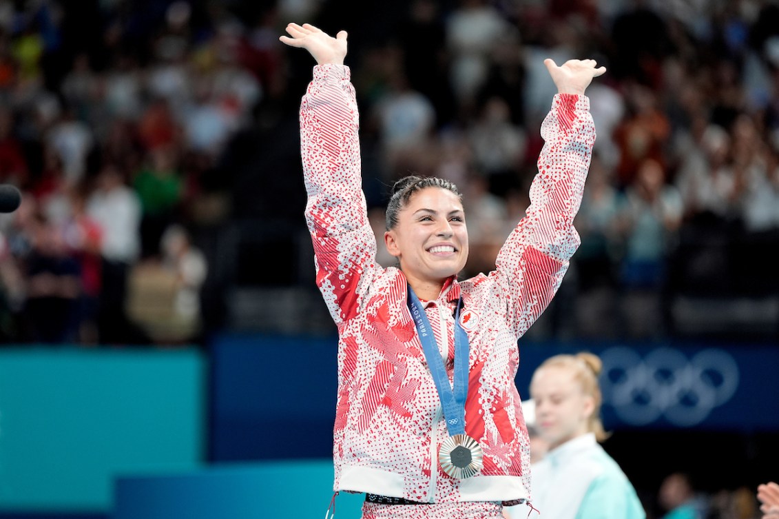 Sophiane Méthot raises her arms while wearing a bronze medal over a red and white track suit