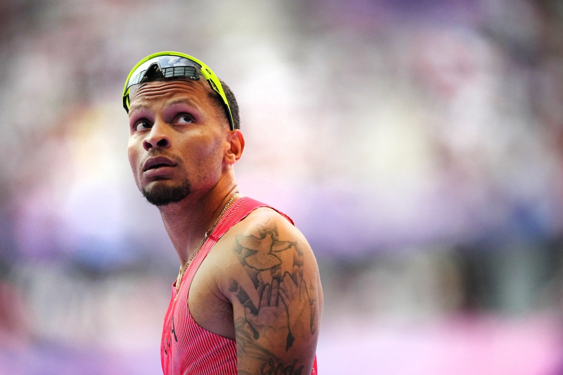 Andre De Grasse looks up while wearing sunglasses on his forehead and a pink singlet