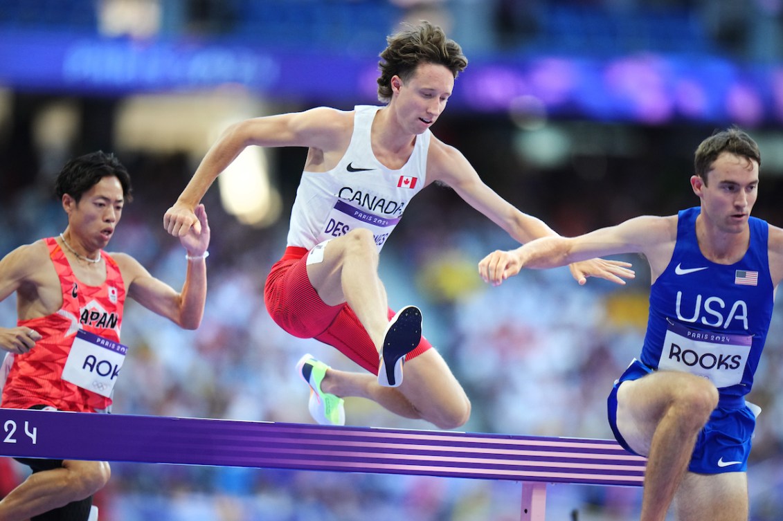 Jean-Simon Desgagnes jumps over a hurdle while wearing a white singlet