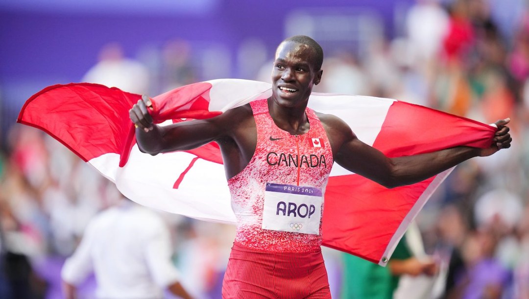 Marco Arop smiles with the Canadian flag flowing behind him