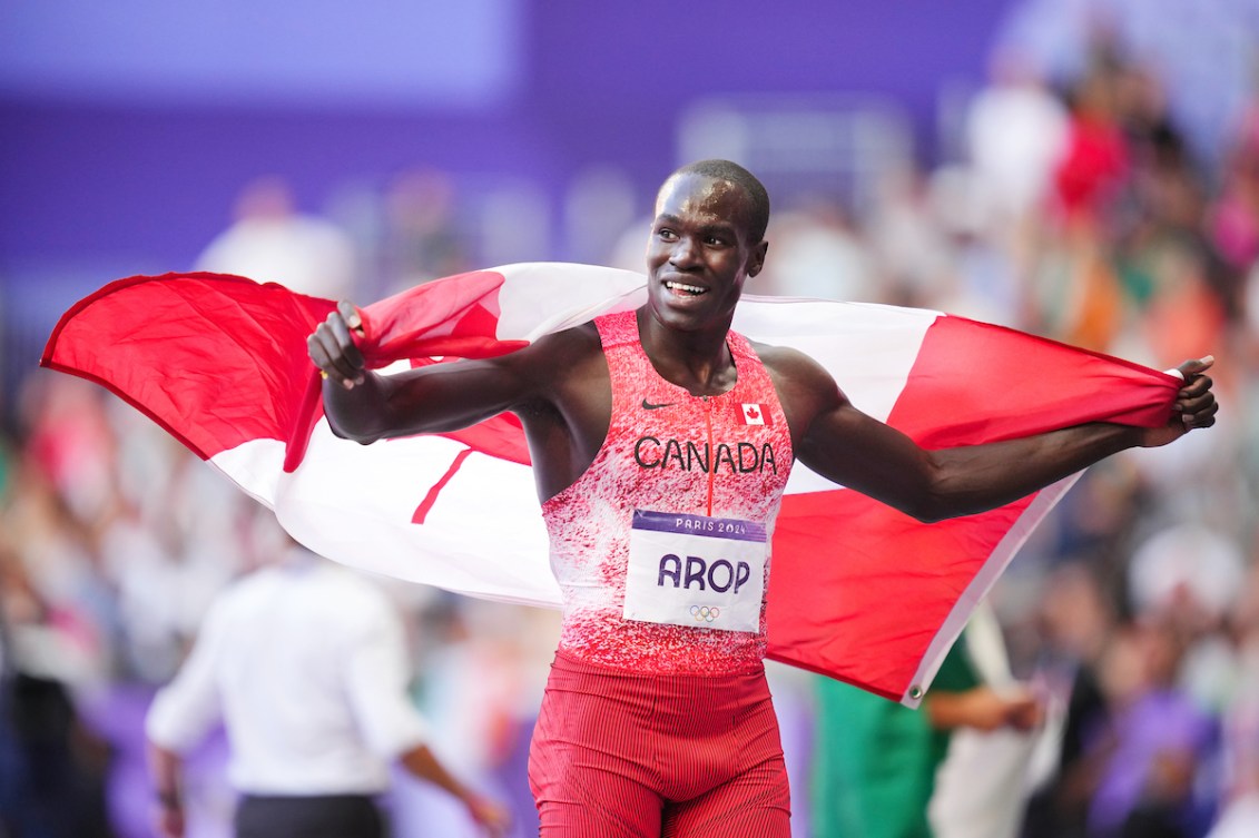 Marco Arop smiles with the Canadian flag flowing behind him 