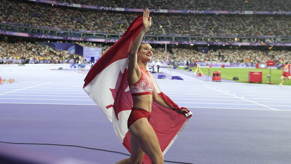 Alysha Newman walks along the track with the Canadian flag draped over her shoulders