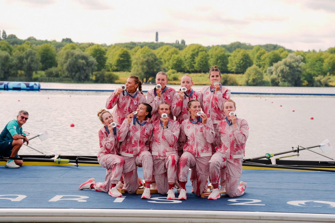 The Canadian women's eight pose with their silver medals while wearing red and white track suits 