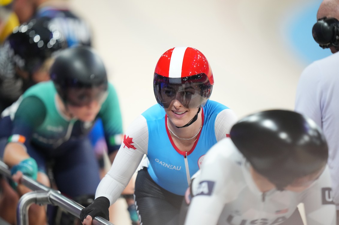 Maggie Coles-Lyster in blue jersey and red helmet hangs onto the side of the velodrome