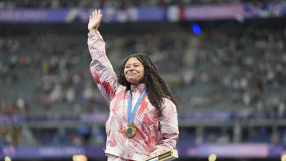 Camryn Rogers raises her arm while standing on the podium wearing a gold medal