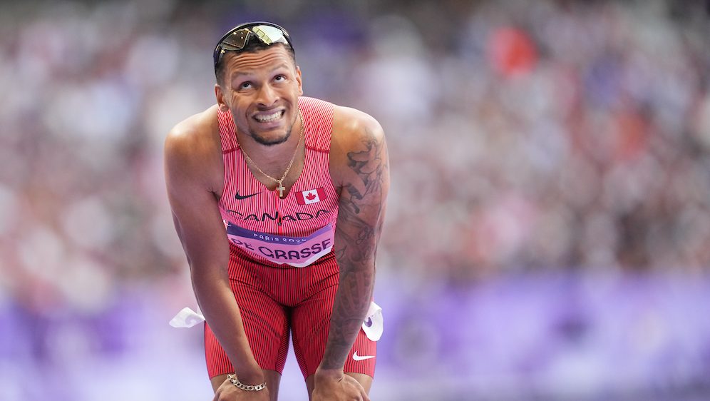 Andre De Grasse leans on his knees after a race 