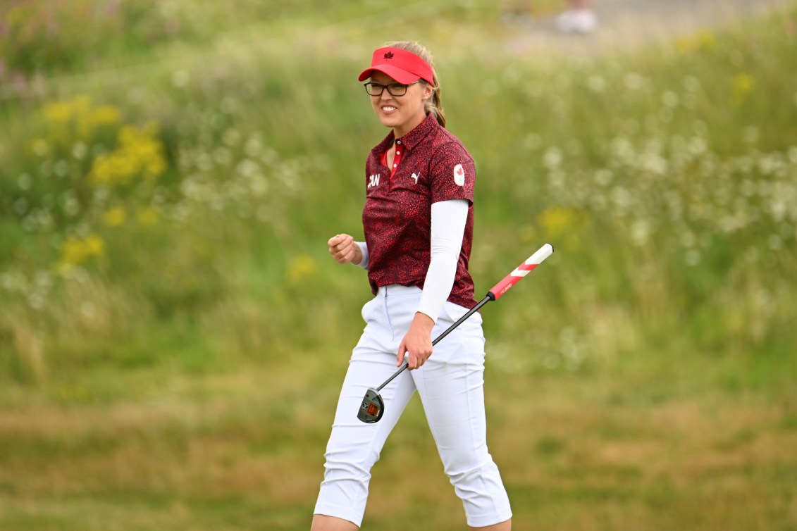 Brooke Henderson fist pumps while wearing a red shirt and white pants