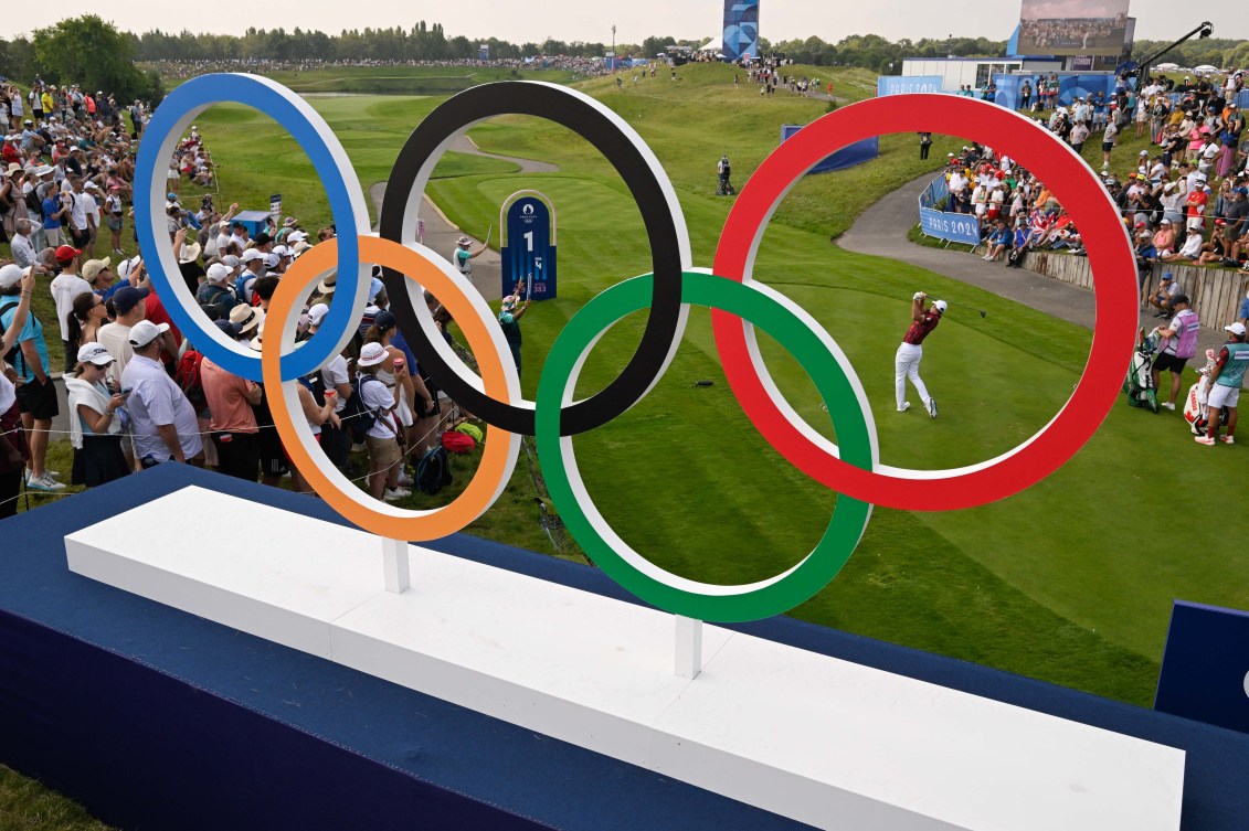 Corey Conners is pictured swinging a golf club through the Olympic rings