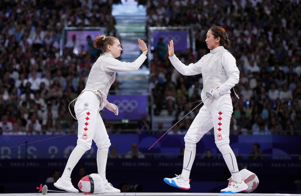 Eleanor Harvey and Yunjia Zhang about to high five in their fencing gear 