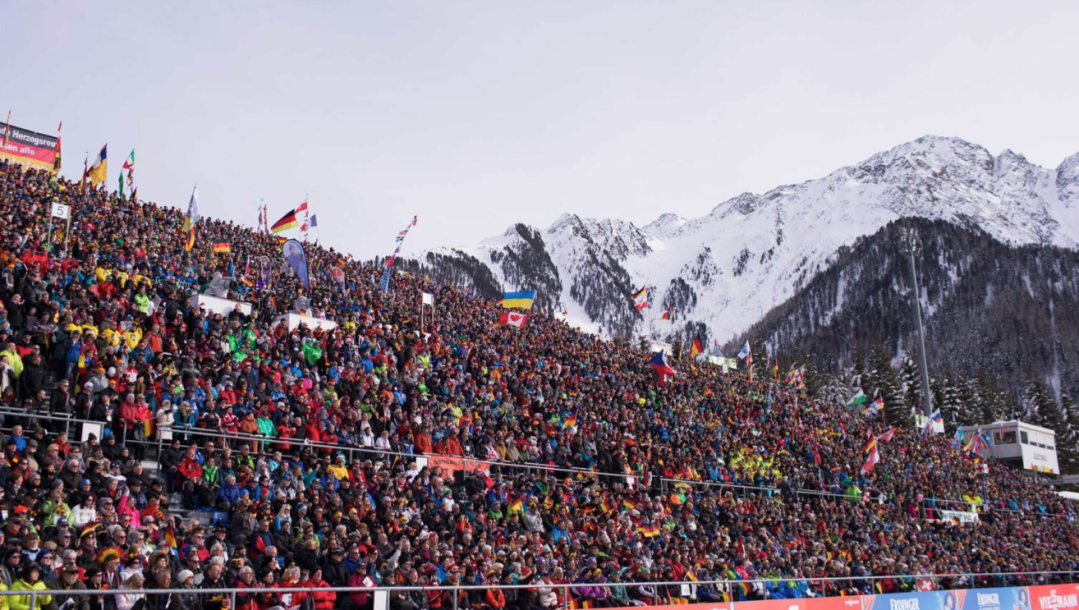 A packed crowd of spectators waves flags with mountains in the background