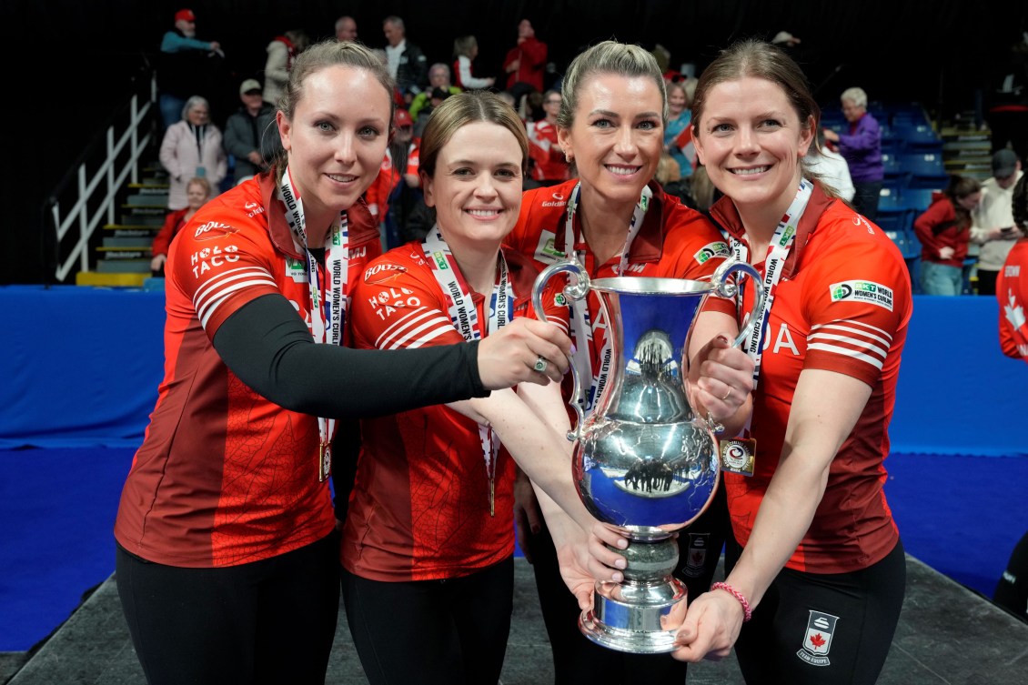 Four women curlers in red shirts and black pants hold the world championship trophy