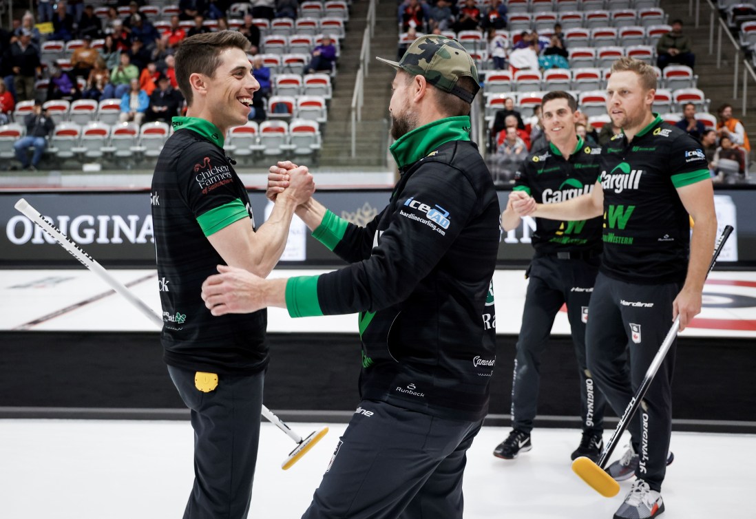 Curlers in black tops and pants with green trim shake hands after a win 