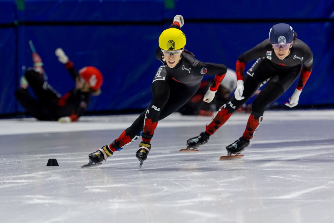 Florence Brunelle in a yellow helmet and black and red suit skates towards the camera in a short track speed skating race