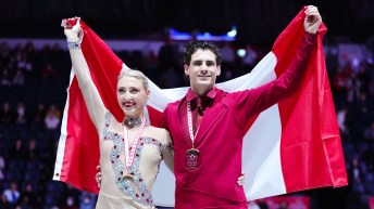 Piper Gilles and Paul Poirier hold the Canadian flag over their shoulders while wearing their medals from Skate Canada International