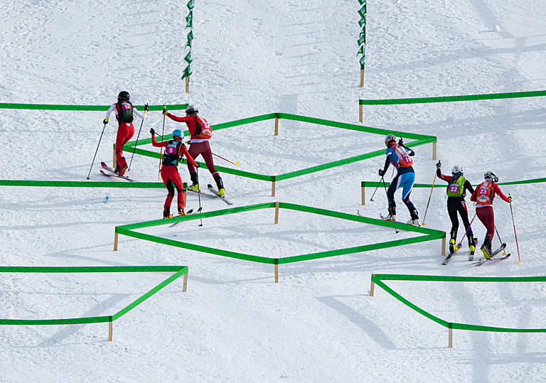 Six ski mountaineering athletes climb up a ski hill around green course markings 