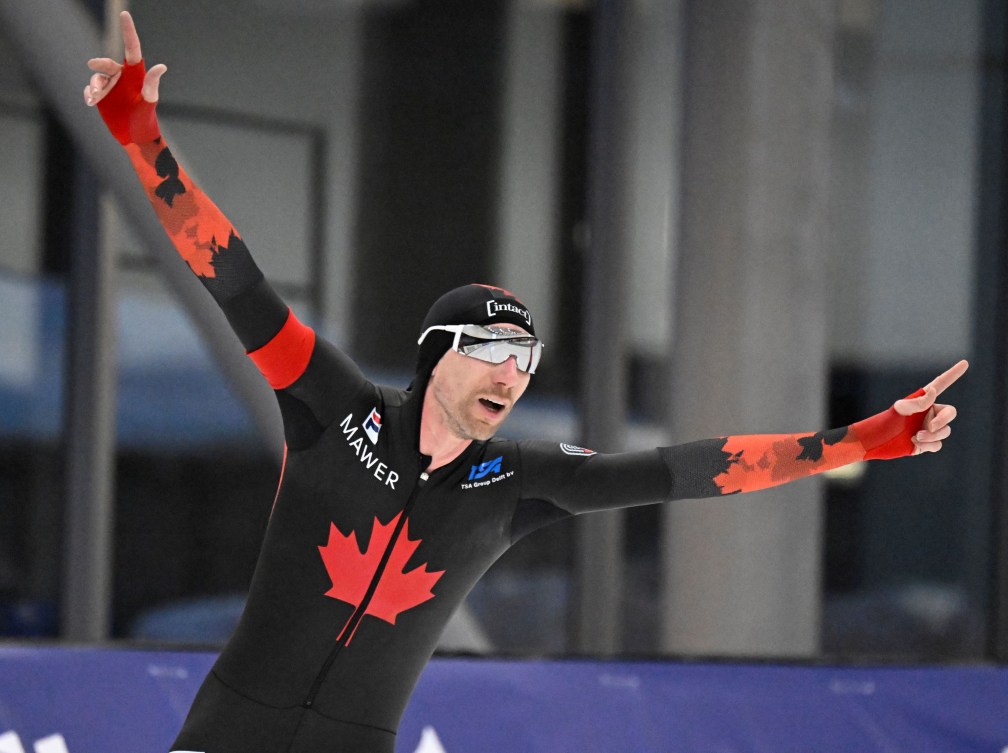 Ted-Jan Bloemen in a black and red skin suit holds his arms out in celebration after a speed skating race