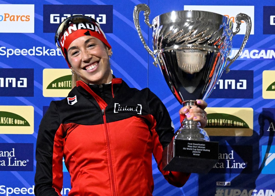 Valerie Maltais smiles as she holds up a silver trophy while wearing a black and red jacket 