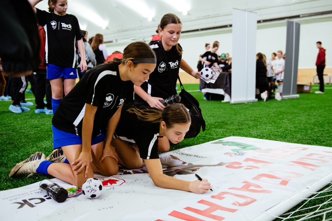 Young athletes pile together on a turf field to sign a banner