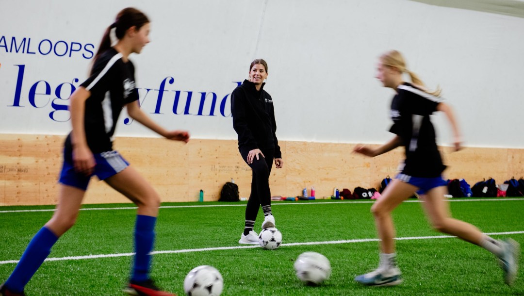 Two young soccer players practice a drill while a coach looks on