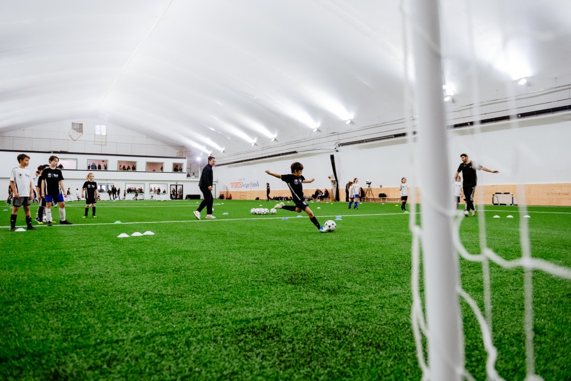 A young boy winds up to kick a soccer ball into the net on an indoor field