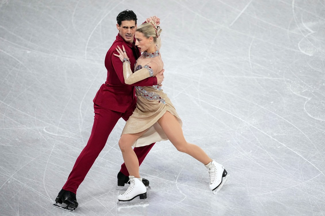 Paul Poirier dressed in a red suit and Piper Gilles in a gold dress dance in tango hold 