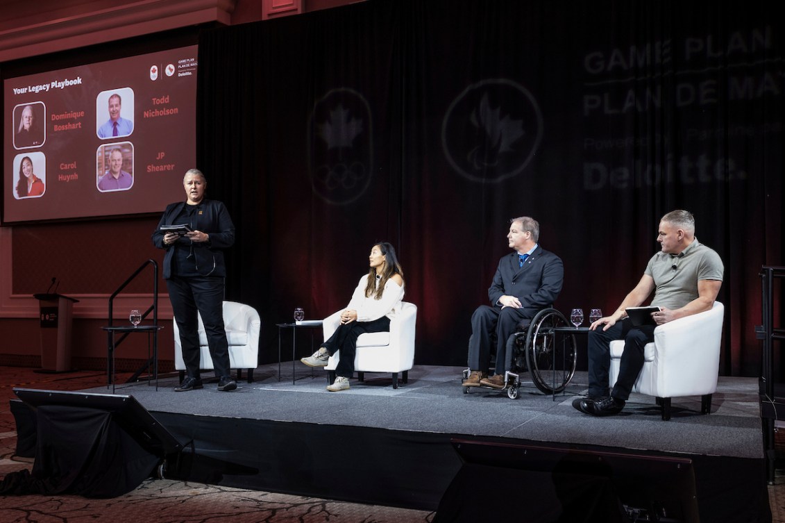 Four panelists sit on a stage talking to attendees