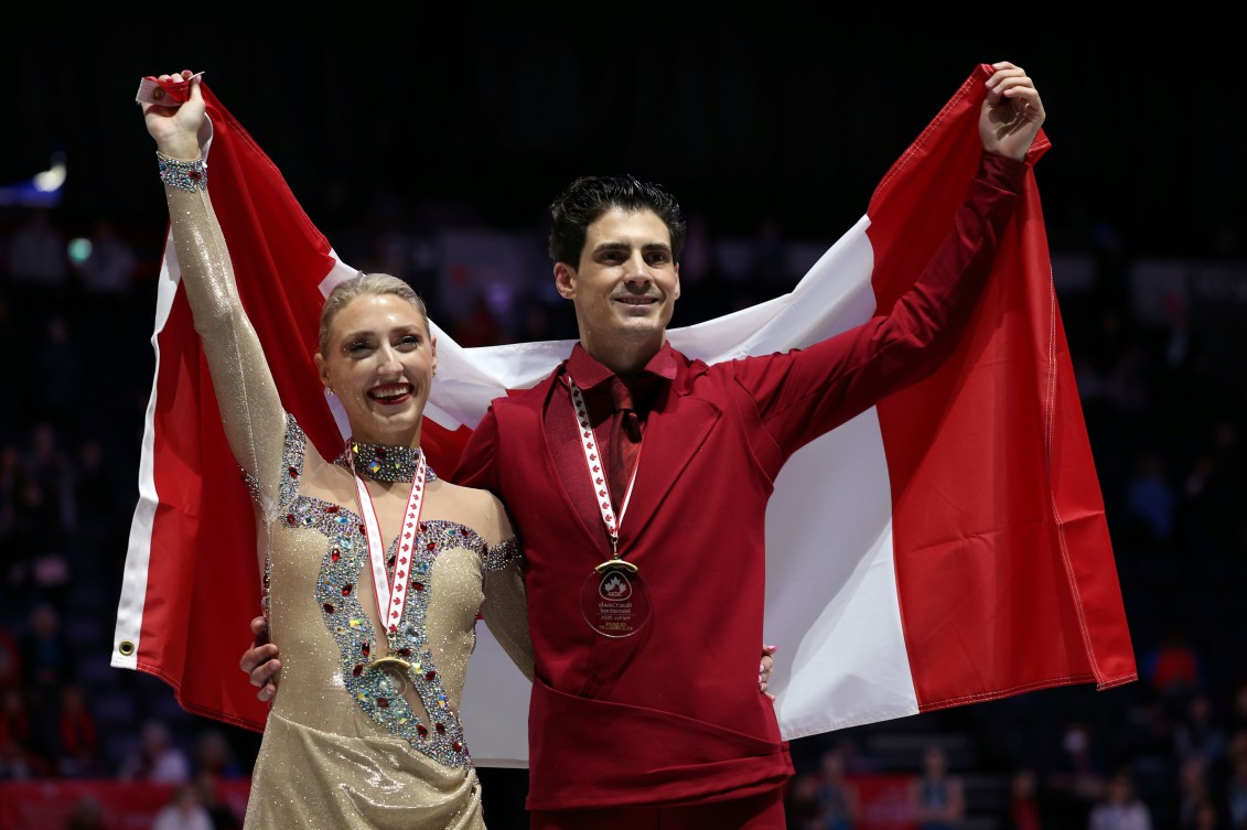 Piper Gilles and Paul Poirier lift a Canadian flag behind their shoulders