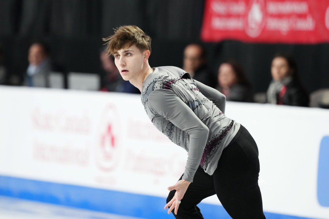 Roman Sadovsky looks over his shoulder as he skates in a grey shirt and black pants 