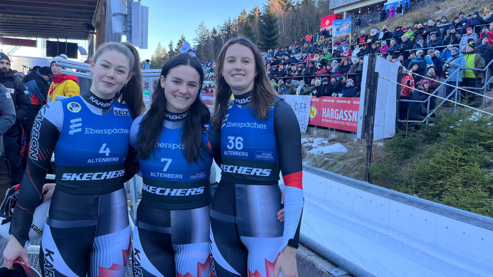 Caitlin Nash, Embyr Lee Susko and Trinity Ellis stand arm in arm beside a luge track