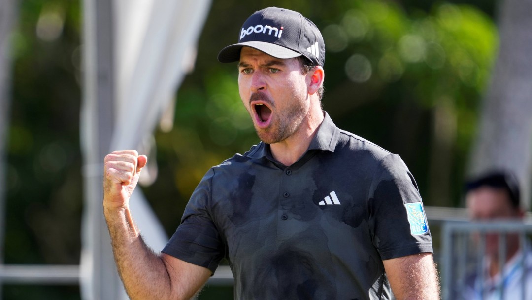 Nick Taylor pumps his fist in celebration while wearing a grey golf shirt and hat