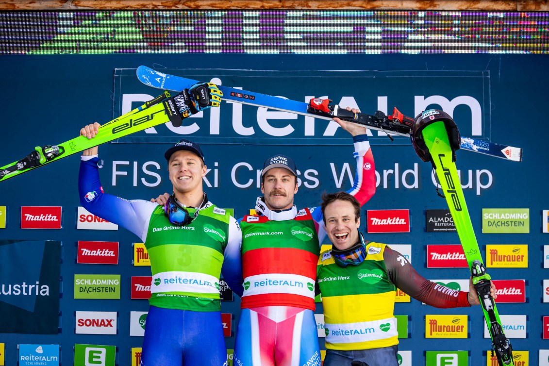 Three athletes hold their skis over their head in celebration